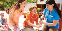 An Adventure Guide helps a young boy stir a vat while his mom watches
