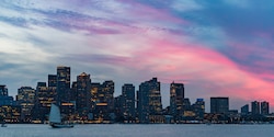 A boat on the Charles River in front of the Boston skyline at dusk