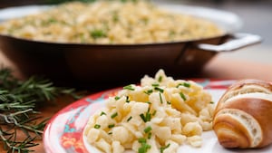 Close-up of a plate of spätzel and a roll and, in the background, a serving bowl of spätzel