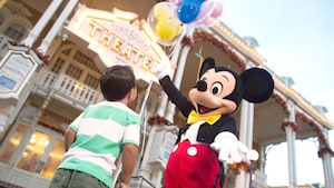 Mickey Mouse holding balloons while welcoming a Guest to Town Square Theater on Main Street, U.S.A.