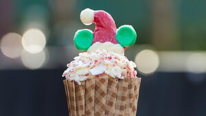 A holiday themed cupcake with a chocolate Mickey ears Santa hat embellishment