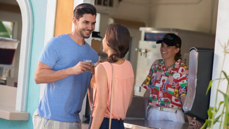 A man and woman smile at each other while holding beverages in front of a concession stand