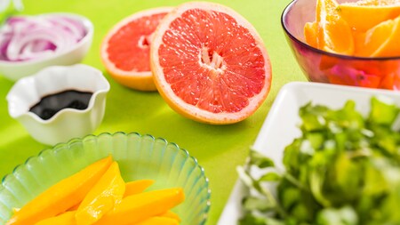 A fresh grapefruit cut in half sits next to other fresh ingredients, including mango and oranges
