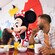 Una niña pequeña roza su nariz con la de Minnie Mouse mientras su hermano y su padre observan durante un desayuno-almuerzo con Personajes
