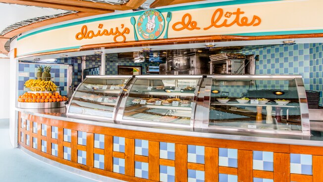 A sign with a portrait of Daisy Duck hangs above a quick service counter with fruit, salads and bakery items