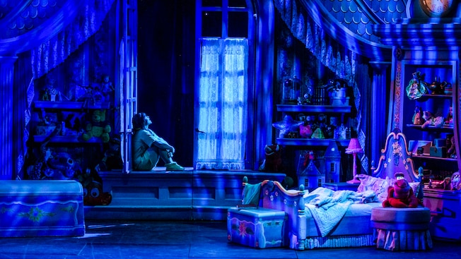 A young girl sits in her open bedroom window at night, imagining the magic of dreams.