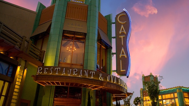 The neon Catal Restaurant & Uva Bar sign lights up as the sun sets over Downtown Disney District