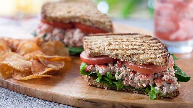 A lobster club sandwich cut in half and potato chips on a wooden palette