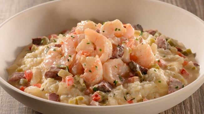 A bowl of shrimp, grits, vegetables, cream sauce, tasso ham and poached eggs