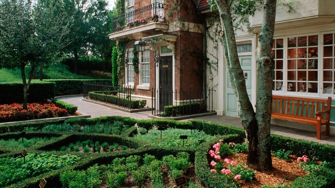 An English themed landscape with a manicured garden next to a brick building with ornate railings