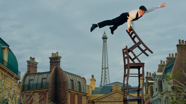 The acrobat member of the two-man Serveur Amusant comedy team balances atop a tower of chairs