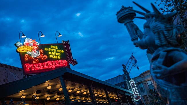 Missy Piggy as the Statue of Liberty nearby an illuminated PizzeRizzo sign featuring Rizzo the Rat