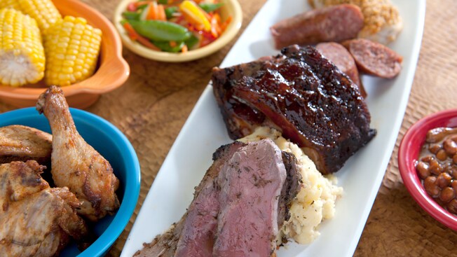 Dinner platter with ribs, chicken, sausage and mashed potatoes, and sides in bowls