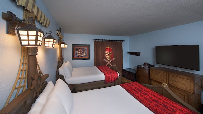 Two pirate ship-themed double beds, TV, dresser, luggage seat and, beyond, a skull curtain to a vanity