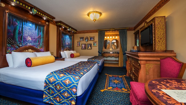 2 royal beds with tall elaborate headboards, elegant dresser and curtained bathroom with vanity