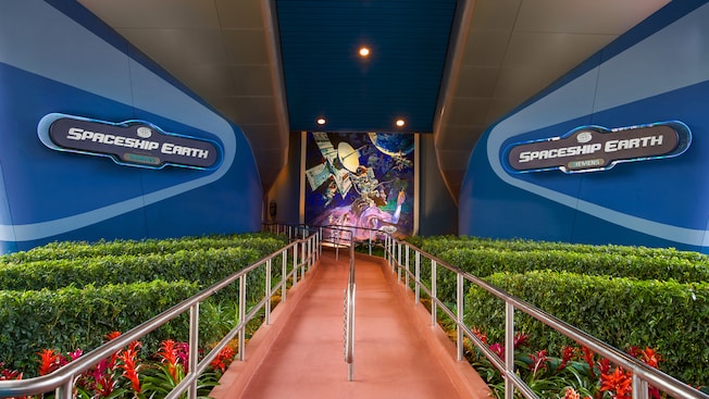 A walkway flanked by 2 wall signs leading up to Spaceship Earth at Epcot