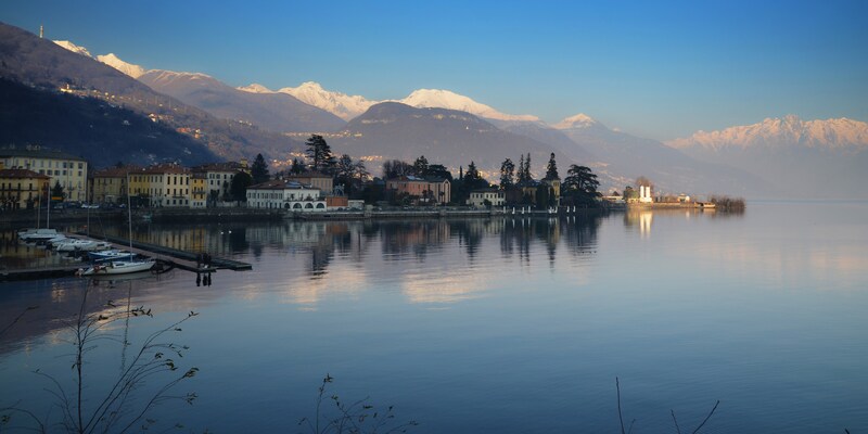 A calm lake reflecting clouds is surrounded by villas and mountains