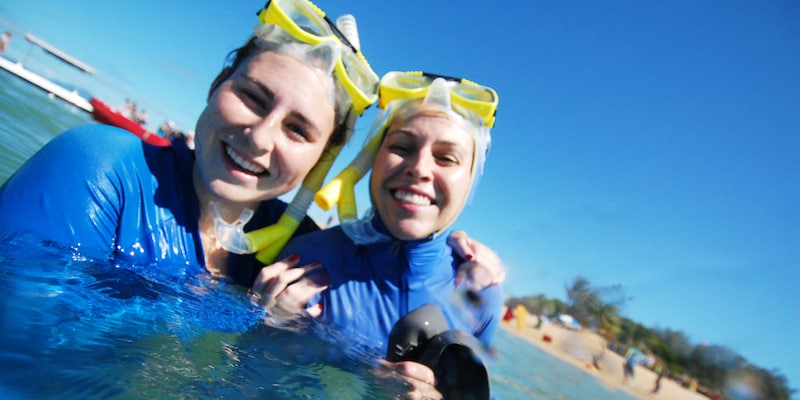 2 smiling teenage girls dressed in wet suits tread water and hold snorkel gear