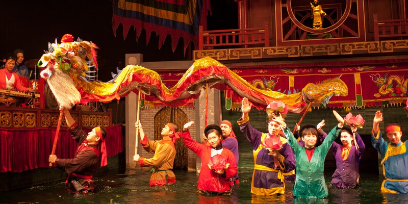 Costumed performers walk through a river carrying a long dragon puppet