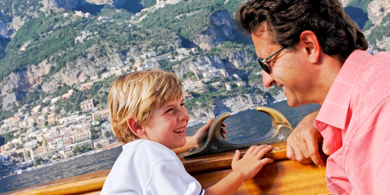 A father and son share a laugh while cruising on a boat along the Italian coast