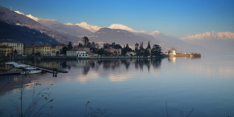 A calm lake reflecting clouds is surrounded by villas and mountains
