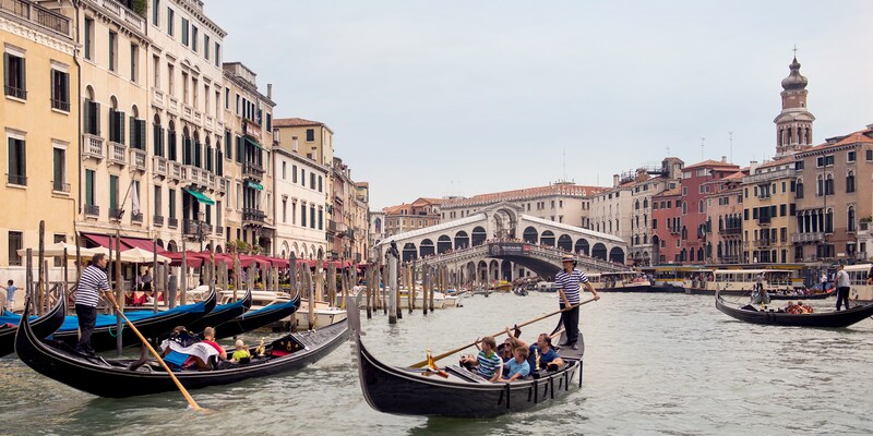 Gondoliers steer several gondolas filled with people on a canal in Venice, Italy