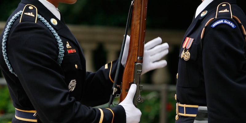 Two Honor Guards at the Arlington National Cemetery, with one holding a rifle as he presents arms