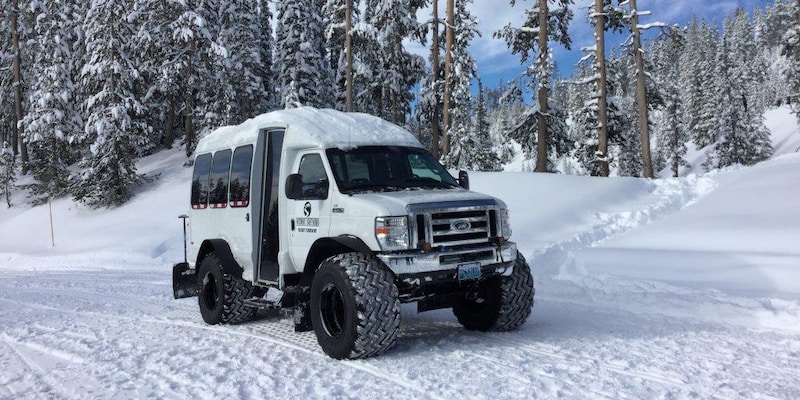A mini snow coach on a snow covered road surrounded by pine trees A mini snow coach on a snow covered road surrounded by pine trees