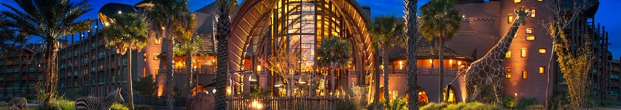The illuminated exterior of Disney’s Animal Kingdom Lodge at night with a giraffe and 2 zebras roaming the grounds