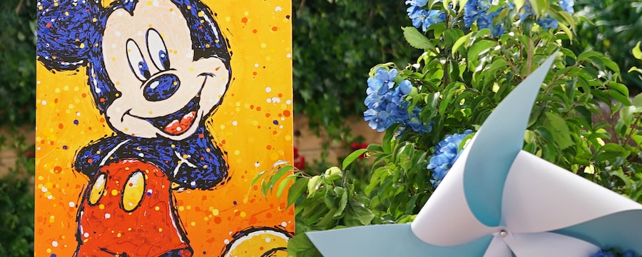 A stylized painting of Mickey Mouse is displayed amongst lush foliage dotted with pinwheels