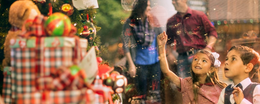 2 young children look in awe at a decorated Christmas tree on display in a shop window