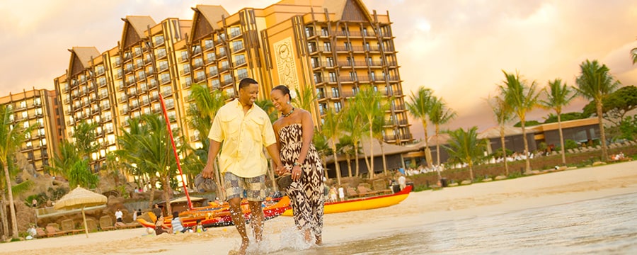 A couple walks along the water's edge at Aulani, Disney Vacation Club Villas in Ko Olina, Hawai'i