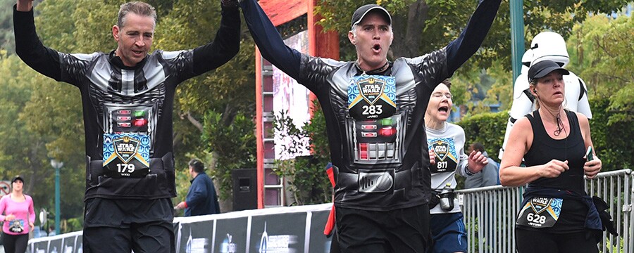 Two runners raise each others hands in victory as they cross the finish line together