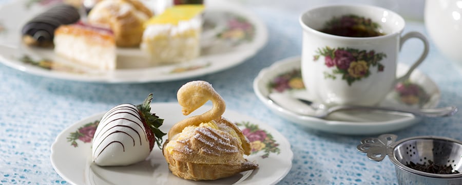 White chocolate-dipped strawberry, swan-shaped scones and black tea on floral English tea service china